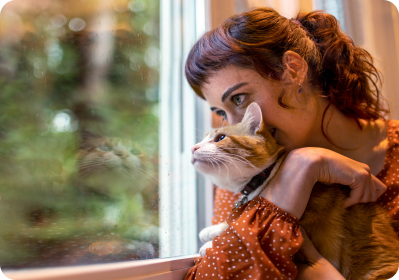 A brown-white cat sitting in a woman's lap looking outside a window